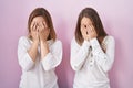 Middle age mother and young daughter standing over pink background with sad expression covering face with hands while crying Royalty Free Stock Photo