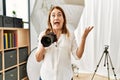 Middle age photography woman using camera at photo studio celebrating victory with happy smile and winner expression with raised Royalty Free Stock Photo