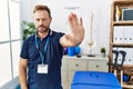 Middle age physiotherapist man working at pain recovery clinic doing stop sing with palm of the hand Royalty Free Stock Photo