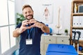 Middle age physiotherapist man working at pain recovery clinic smiling in love doing heart symbol shape with hands Royalty Free Stock Photo