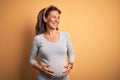 Middle age pregnant woman expecting baby at aged pregnancy looking away to side with smile on face, natural expression Royalty Free Stock Photo