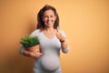 Middle age pregnant woman expecting baby holding plant pot happy with big smile doing ok sign, thumb up with fingers, excellent Royalty Free Stock Photo