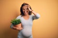 Middle age pregnant woman expecting baby holding plant pot with happy face smiling doing ok sign with hand on eye looking through Royalty Free Stock Photo