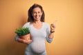 Middle age pregnant woman expecting baby holding plant pot very happy pointing with hand and finger to the side Royalty Free Stock Photo