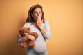 Middle age pregnant woman expecting baby holding teddy bear stuffed animal cover mouth with hand shocked with shame for mistake, Royalty Free Stock Photo