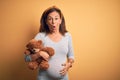 Middle age pregnant woman expecting baby holding teddy bear stuffed animal scared in shock with a surprise face, afraid and Royalty Free Stock Photo