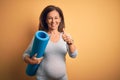 Middle age pregnant woman expecting baby holding yoga mat for healthy lifestyle happy with big smile doing ok sign, thumb up with Royalty Free Stock Photo