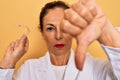 Middle age senior dentist woman holding clear aligner for teeth correction with angry face, negative sign showing dislike with