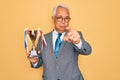 Middle age senior grey-haired business man wearing glasses holding winner trophy pointing with finger to the camera and to you, Royalty Free Stock Photo