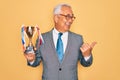 Middle age senior grey-haired business man wearing glasses holding winner trophy pointing and showing with thumb up to the side Royalty Free Stock Photo