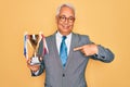 Middle age senior grey-haired business man wearing glasses holding winner trophy with surprise face pointing finger to himself Royalty Free Stock Photo