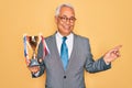 Middle age senior grey-haired business man wearing glasses holding winner trophy very happy pointing with hand and finger to the Royalty Free Stock Photo