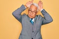 Middle age senior grey-haired handsome business man wearing glasses over yellow background Doing bunny ears gesture with hands Royalty Free Stock Photo