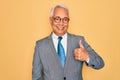 Middle age senior grey-haired handsome business man wearing glasses over yellow background doing happy thumbs up gesture with hand Royalty Free Stock Photo