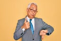 Middle age senior grey-haired handsome business man wearing glasses over yellow background Doing thumbs up and down, disagreement Royalty Free Stock Photo