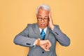 Middle age senior grey-haired handsome business man wearing glasses over yellow background Looking at the watch time worried, Royalty Free Stock Photo