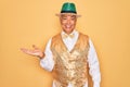 Middle age senior grey-haired man wearing Brazilian carnival custome over yellow background smiling cheerful presenting and