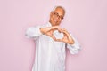 Middle age senior grey-haired man wearing glasses and business shirt over pink background smiling in love doing heart symbol shape Royalty Free Stock Photo