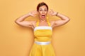 Middle age senior pin up woman wearing 50s style retro dress over yellow background Crazy and scared with hands on head, afraid Royalty Free Stock Photo