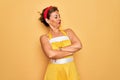 Middle age senior pin up woman wearing 50s style retro dress over yellow background looking to the side with arms crossed Royalty Free Stock Photo