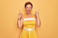 Middle age senior pin up woman wearing 50s style retro dress over yellow background shouting with crazy expression doing rock Royalty Free Stock Photo