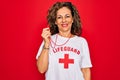 Middle age senior summer lifeguard woman holding whistle over red background with a happy and cool smile on face