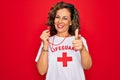 Middle age senior summer lifeguard woman holding whistle over red background pointing fingers to camera with happy and funny face