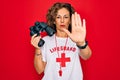 Middle age senior summer lifeguard woman looking through binoculars over red background with open hand doing stop sign with