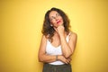 Middle age senior woman with curly hair standing over yellow isolated background with hand on chin thinking about question, Royalty Free Stock Photo