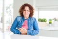 Middle age senior woman with curly hair wearing denim jacket at home with hand on stomach because indigestion, painful illness