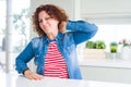 Middle age senior woman with curly hair wearing denim jacket at home Suffering of neck ache injury, touching neck with hand, Royalty Free Stock Photo