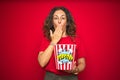 Middle age senior woman eating popcorn snack over red isolated background cover mouth with hand shocked with shame for mistake,