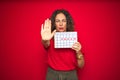 Middle age senior woman holding menstruation calendar over red isolated background with open hand doing stop sign with serious and