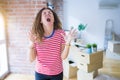 Middle age senior woman moving to a new house packing cardboard boxes crazy and mad shouting and yelling with aggressive