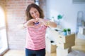 Middle age senior woman moving to a new house packing cardboard boxes smiling in love showing heart symbol and shape with hands