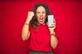 Middle age senior woman showing screen of smartphone over red isolated background annoyed and frustrated shouting with anger, Royalty Free Stock Photo