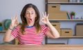 Middle age senior woman sitting at the table at home looking surprised and shocked doing ok approval symbol with fingers Royalty Free Stock Photo