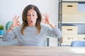 Middle age senior woman sitting at the table at home looking surprised and shocked doing ok approval symbol with fingers Royalty Free Stock Photo