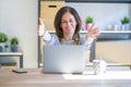 Middle age senior woman sitting at the table at home working using computer laptop looking at the camera smiling with open arms Royalty Free Stock Photo