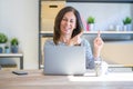 Middle age senior woman sitting at the table at home working using computer laptop smiling and looking at the camera pointing with Royalty Free Stock Photo