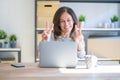 Middle age senior woman sitting at the table at home working using computer laptop smiling looking to the camera showing fingers Royalty Free Stock Photo