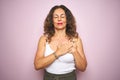 Middle age senior woman standing over pink isolated background smiling with hands on chest with closed eyes and grateful gesture Royalty Free Stock Photo