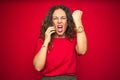 Middle age senior woman talking on the phone over red isolated background annoyed and frustrated shouting with anger, crazy and Royalty Free Stock Photo