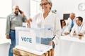 Middle age voter woman smiling happy putting vote in voting box at electoral center