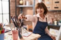 Middle age woman artist smiling confident holding paintbrushe at art studio