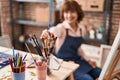 Middle age woman artist smiling confident holding paintbrushe at art studio