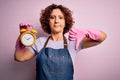 Middle age woman cleaning doing housework wearing apron and gloves holding alarm clock with angry face, negative sign showing