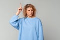 Middle age woman with curly blonde hair in trendy blue sweatshirt having some great idea, lady pointing finger up, standing over Royalty Free Stock Photo