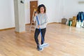 Middle age woman with curly hair working cleaning the house using a broom brush, doing domestic housework chores on new home Royalty Free Stock Photo