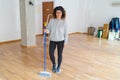 Middle age woman with curly hair working cleaning the house using a broom brush, doing domestic housework chores on new home Royalty Free Stock Photo